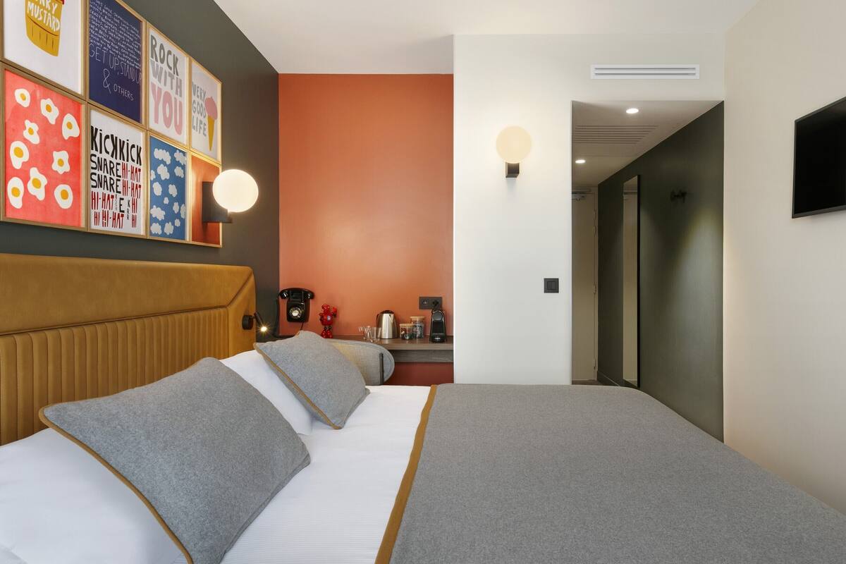 Een hotelkamer met een bed, hoofdbord, een aan de muur bevestigde televisie, nachtkastje met lamp en een muur met kleurrijke kunstwerken.