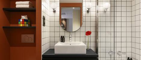 A modern bathroom with a white sink, black countertop, and a large mirror. There are shelves with towels and a Rubik's cube.