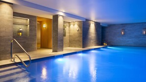 A modern indoor swimming pool with a clear water surface, surrounded by stone walls and recessed lighting.
