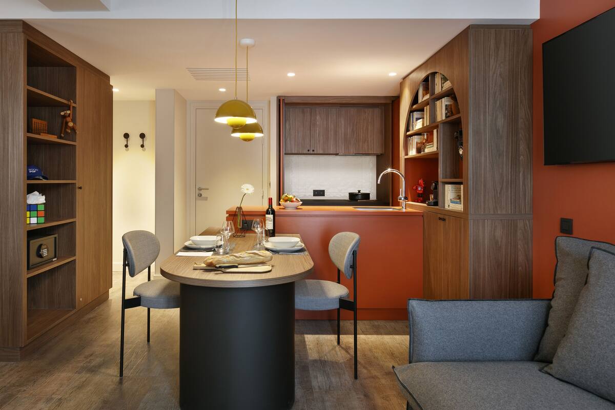 Een moderne keuken met houten kastjes, een eethoek met een ronde tafel, en een inbouwboekenplank.