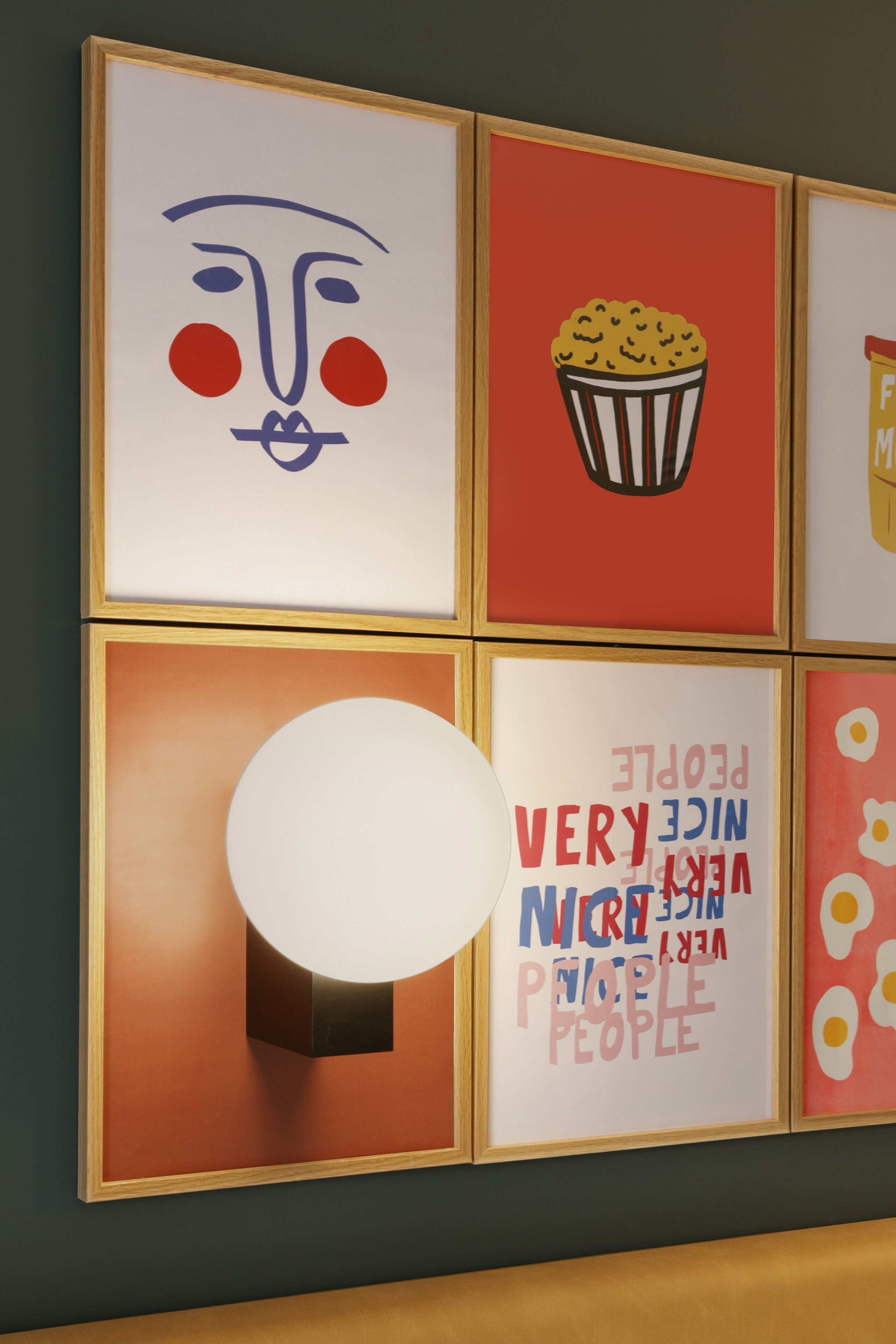 A wall with framed artwork, including a face, a popcorn bucket, and a light fixture.
