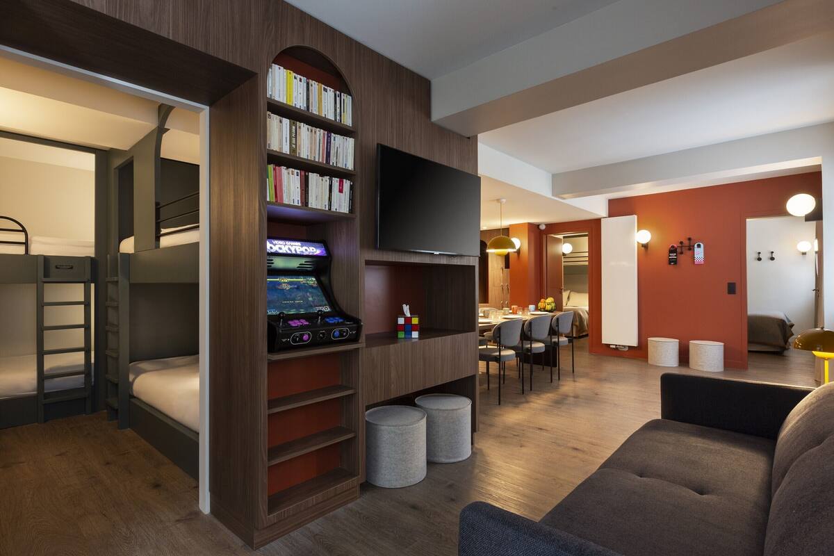 Een moderne hotelkamer met een stapelbed, een flatscreen-tv, een boekenplank en een zithoek.