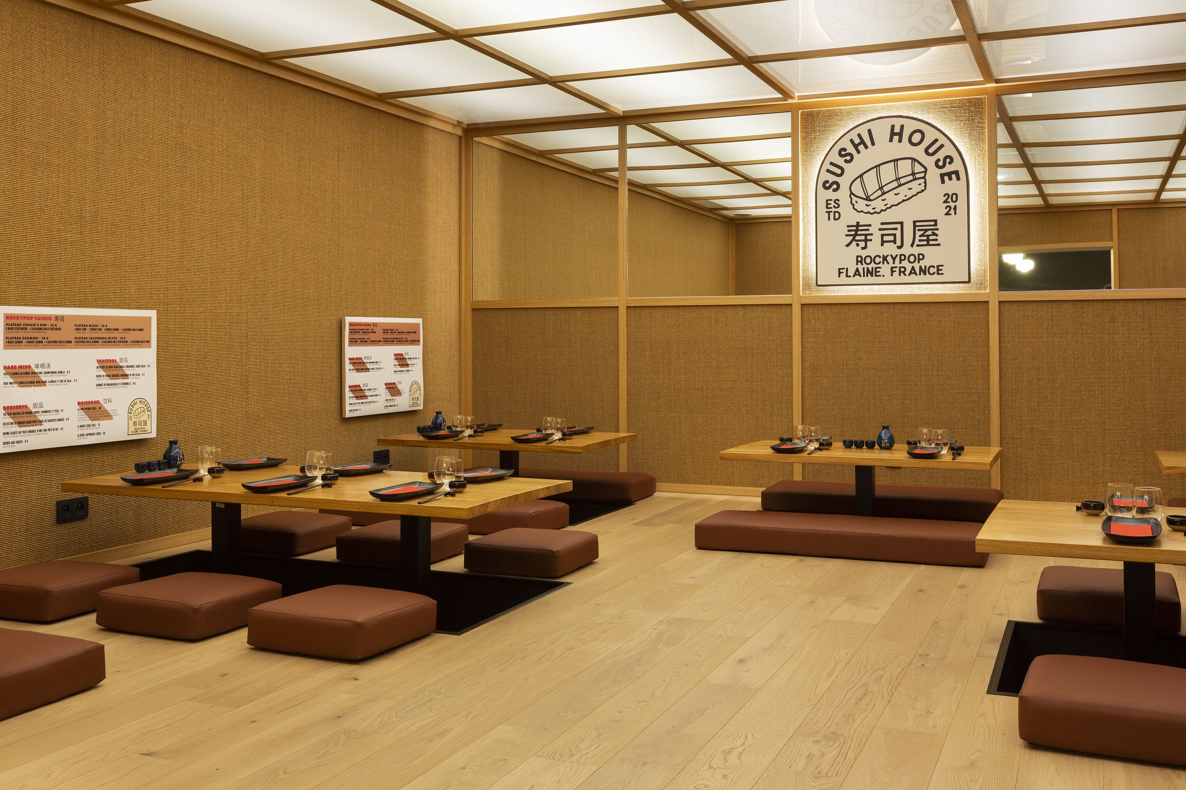 Un restaurante de sushi con varias mesas y cabinas, suelo de madera y un cartel que indica que es una casa de sushi.