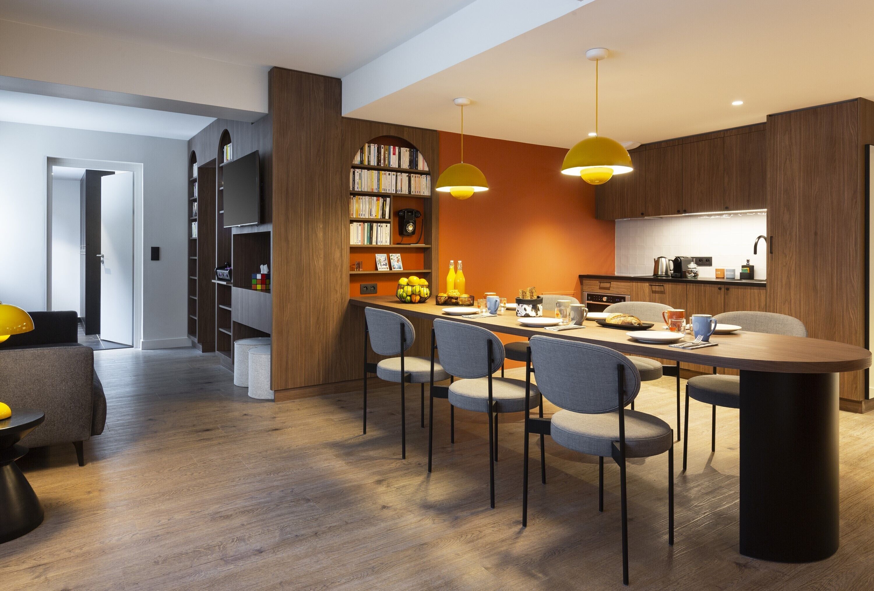 A modern kitchen with wooden cabinets, a dining table with chairs, and pendant lighting.