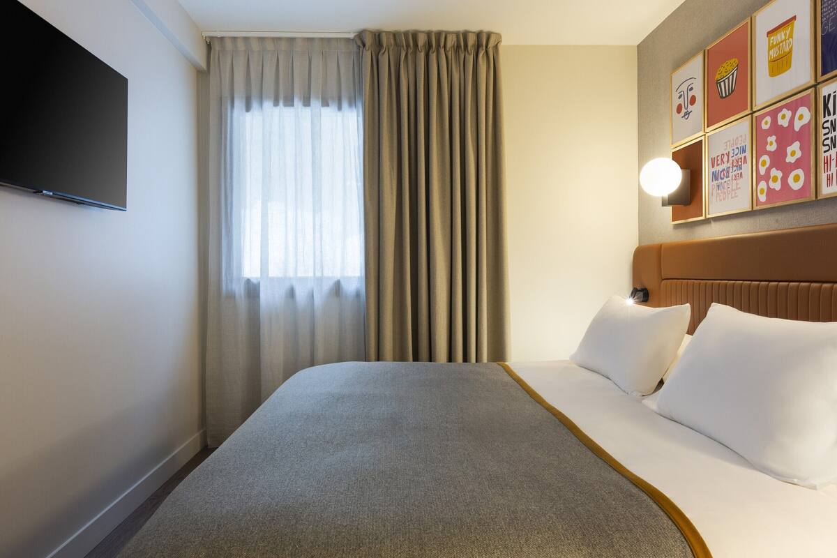 Een hotelkamer met een groot bed, een flatscreen televisie aan de muur, een raam met gordijnen en een muur met kleurrijke kunstwerken.