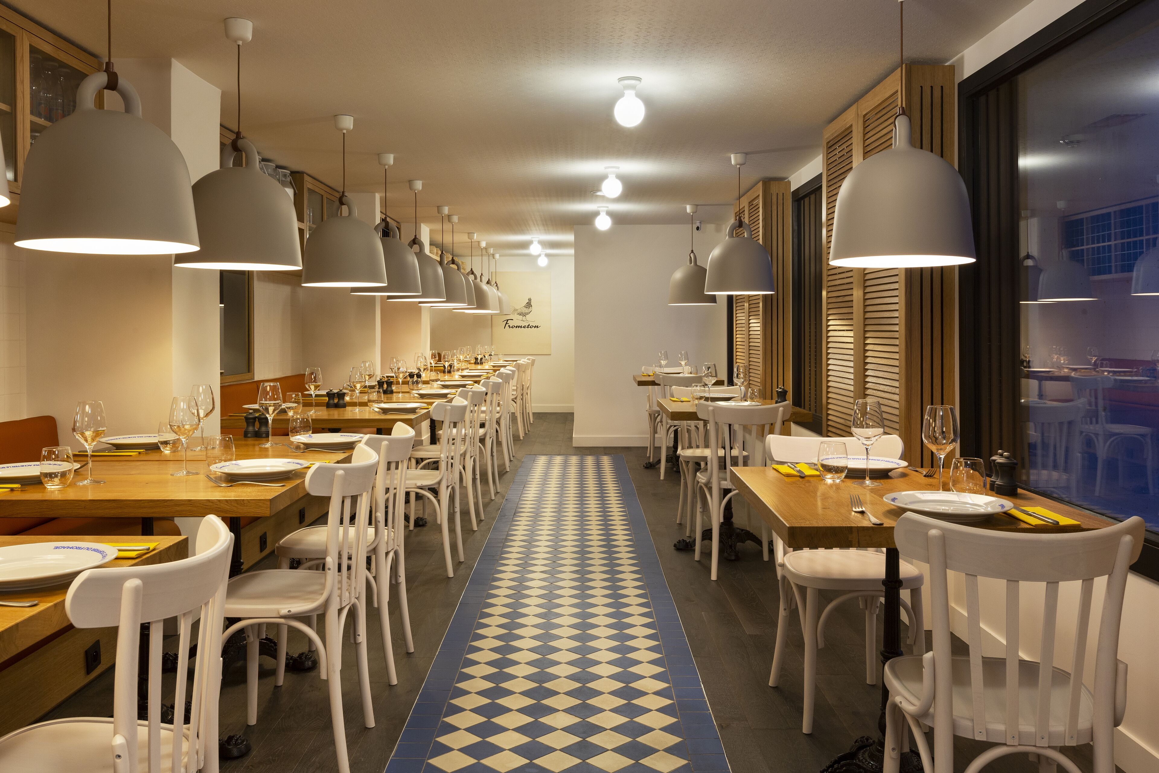 A dining area with multiple tables and chairs, overhead lighting, and a patterned floor.