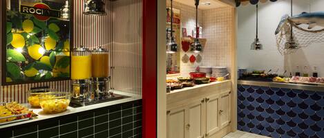 A kitchen area with a buffet setup, including a fruit bowl, a juice dispenser, and various food items on the counter.
