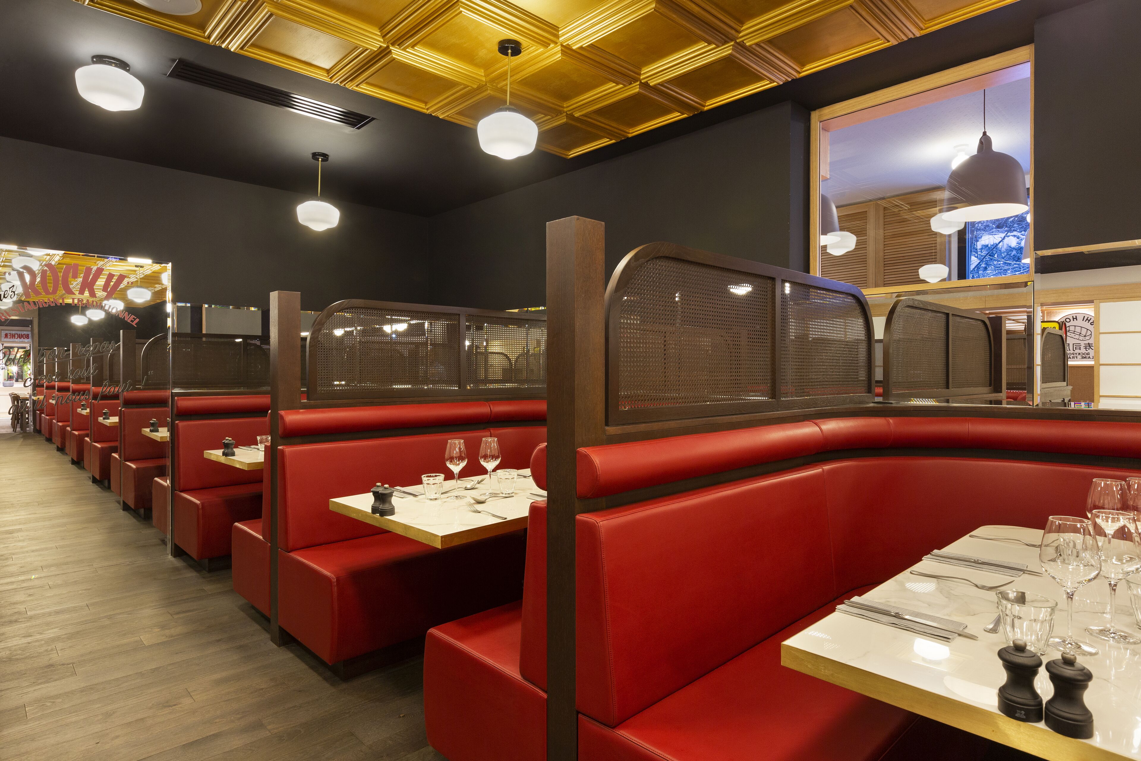 A restaurant interior with red booths, wooden tables, and pendant lighting.