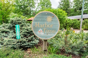 A circular sign with the text "Harbor Time" and a sailboat graphic, surrounded by greenery.