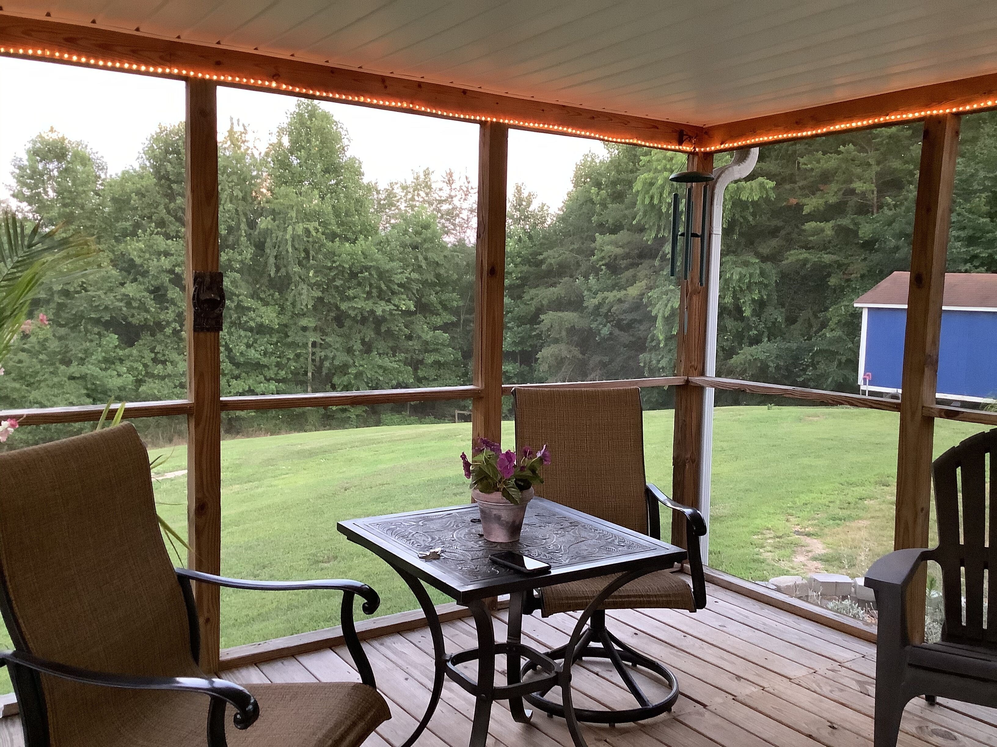 Un espace extérieur abrité, avec une table et des chaises, donnant sur une cour verdoyante et des arbres.