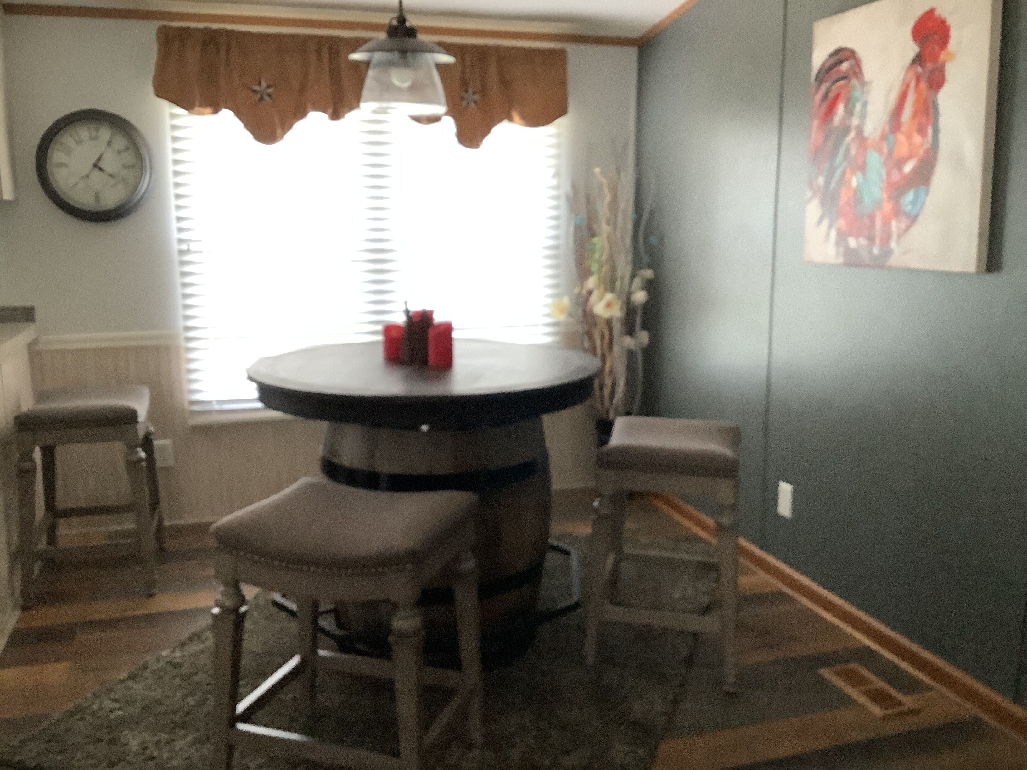 A dining area with a round table, two chairs, a clock on the wall, and a window with blinds.