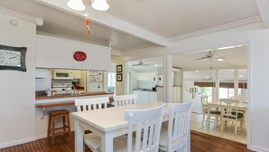 A modern kitchen with white cabinetry, a wooden countertop, and a dining area with white chairs and a table. - Cape Haus Extra (Port St. Joe)