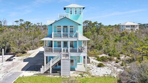 Une maison de plage à deux étages, dotée d’un balcon et d’une petite tour.