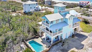 Une maison à plusieurs étages avec une piscine, entourée d’arbres et offrant une vue sur la plage.