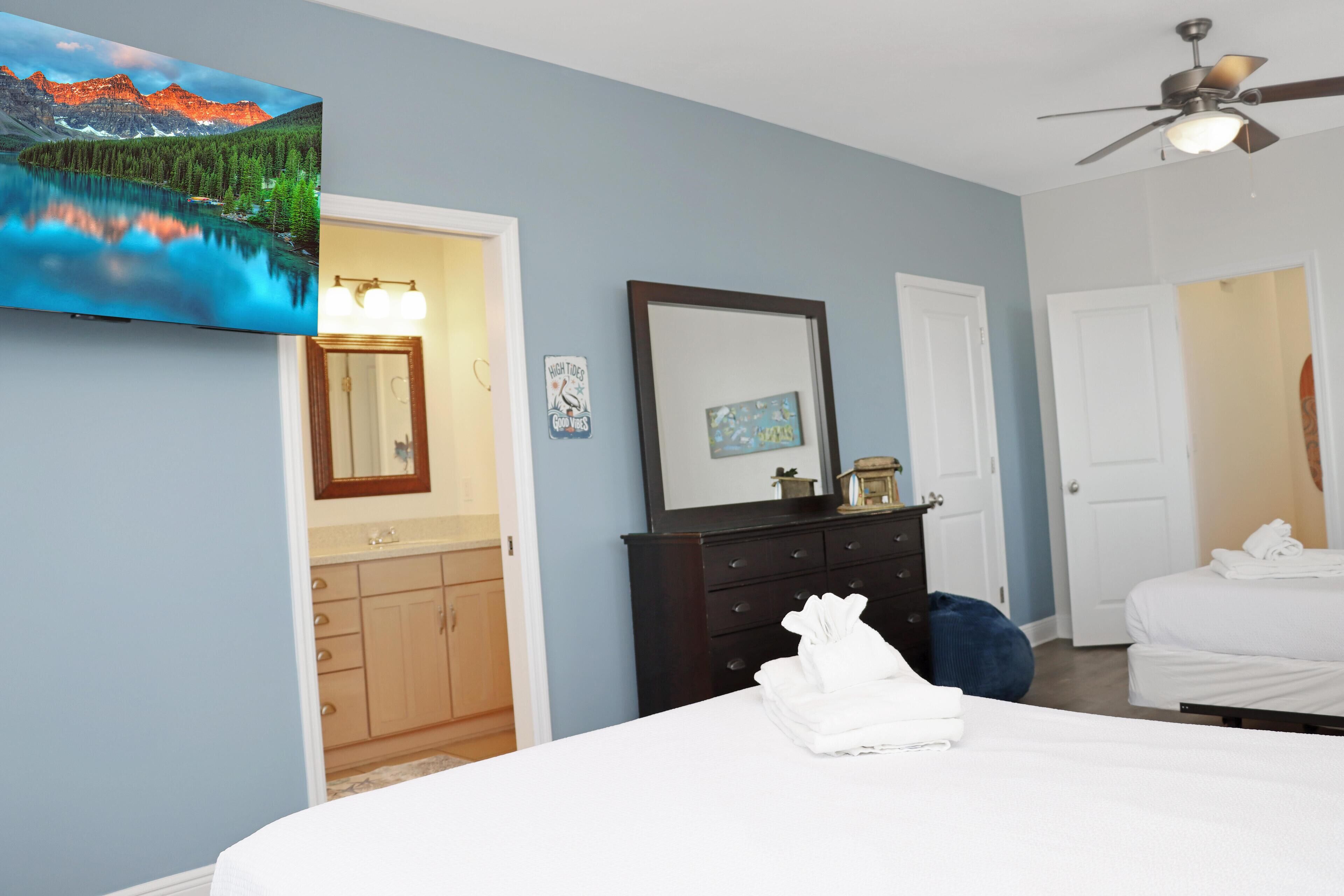 Une chambre à coucher avec un lit, une commode, un miroir et un téléviseur fixé au mur.