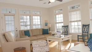 Un salon spacieux avec un canapé beige, un pouf à motifs, une table basse blanche et deux fauteuils bleus.