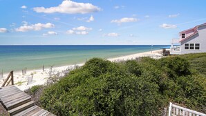A beach view with a wooden deck leading to a white building with a red roof. - Cape Destiny (Port St. Joe)
