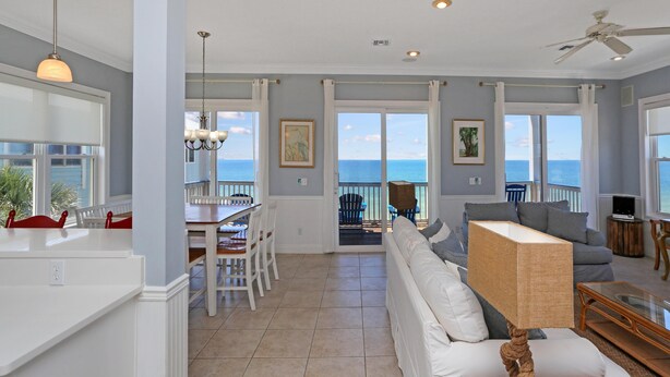 A spacious living area with a large window overlooking the ocean, a dining area with white furniture, and a cozy seating area with a white sofa and a unique lamp. - Cape Destiny (Port St. Joe)