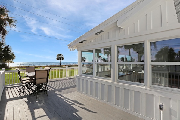 A covered outdoor deck with a table and chairs, overlooking a beach.
