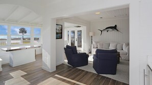 Amplia sala de estar con vista al océano, una cocina blanca y un comedor con una barra alargada.