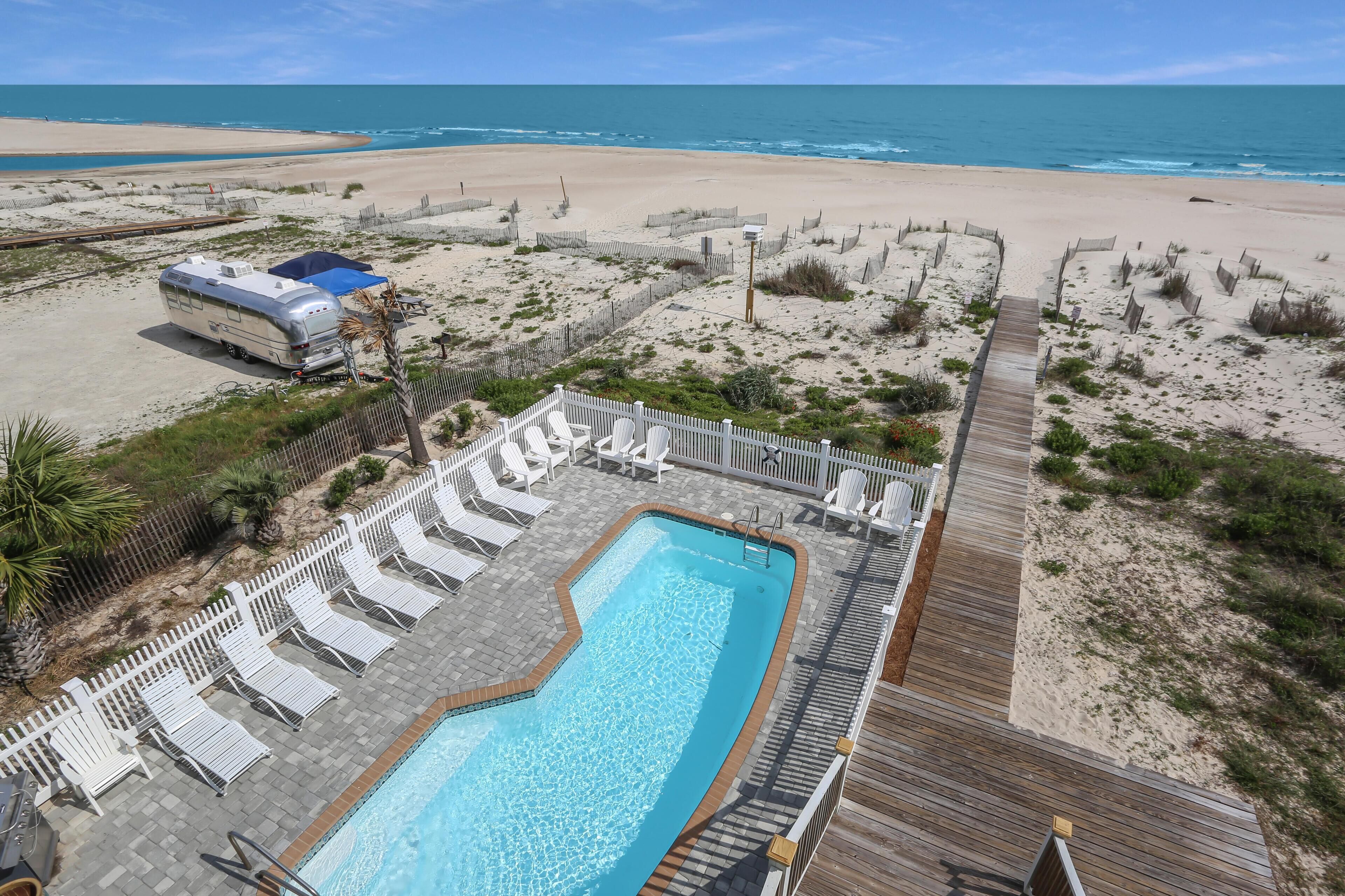 Area piscina con pavimento in legno, lettini e vista sulla spiaggia e sull'oceano.