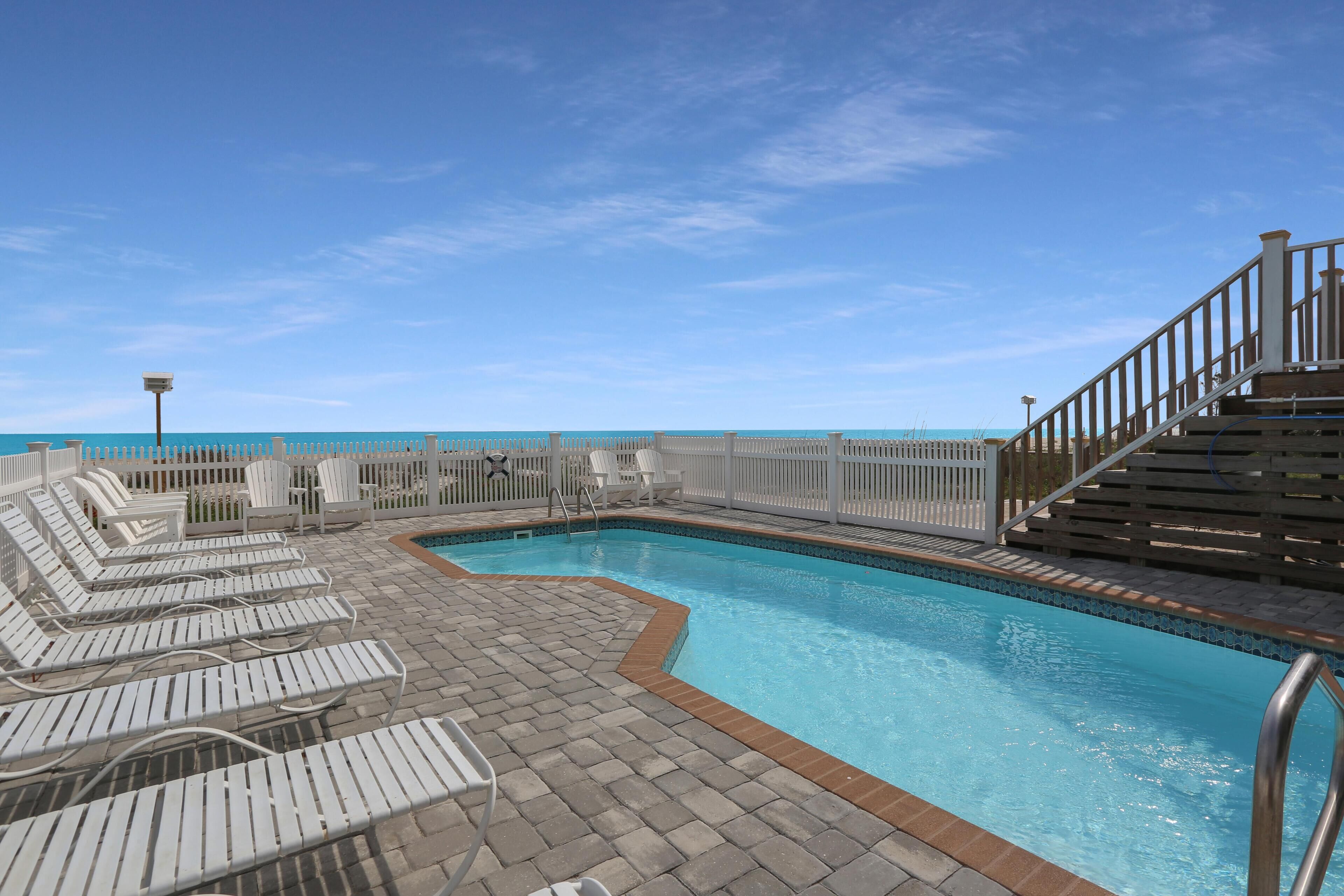Zona de piscina con sillones de descanso y una terraza de madera.