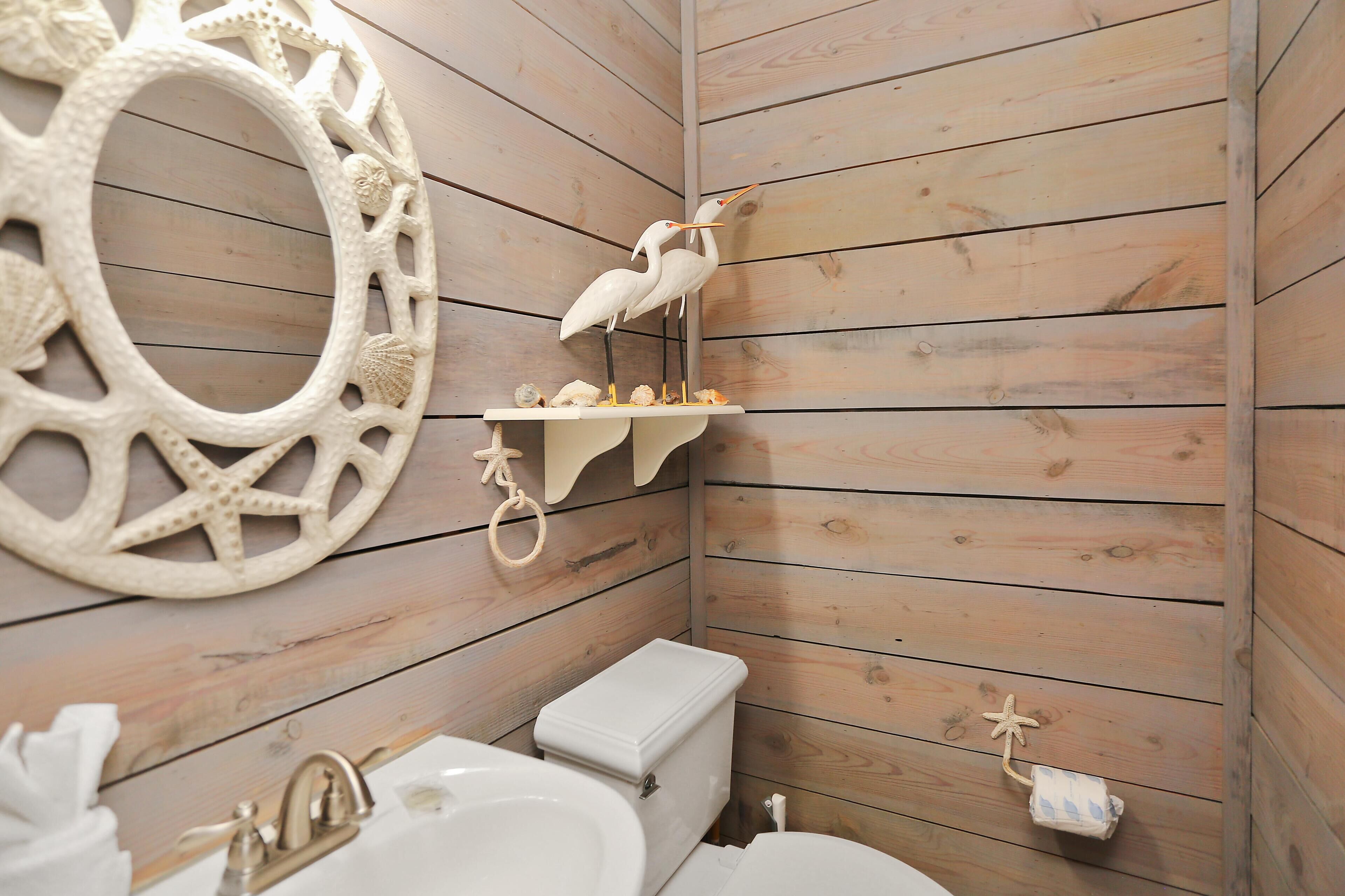 Bagno con rivestimento in legno, un lavandino bianco, un water e decorazioni a parete, tra cui una stella marina e due uccelli bianchi.