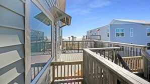 A wooden deck with a glass balustrade overlooking a beach, adjacent to a building with a white facade and blue windows. - Coastal Sunshine (Port St. Joe)