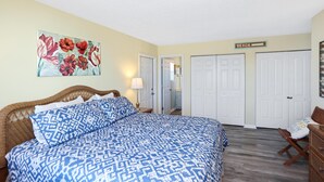 A bedroom with a bed, a painting, a 'BEACH' sign, and a door leading to another room. - Coastal Sunshine (Port St. Joe)
