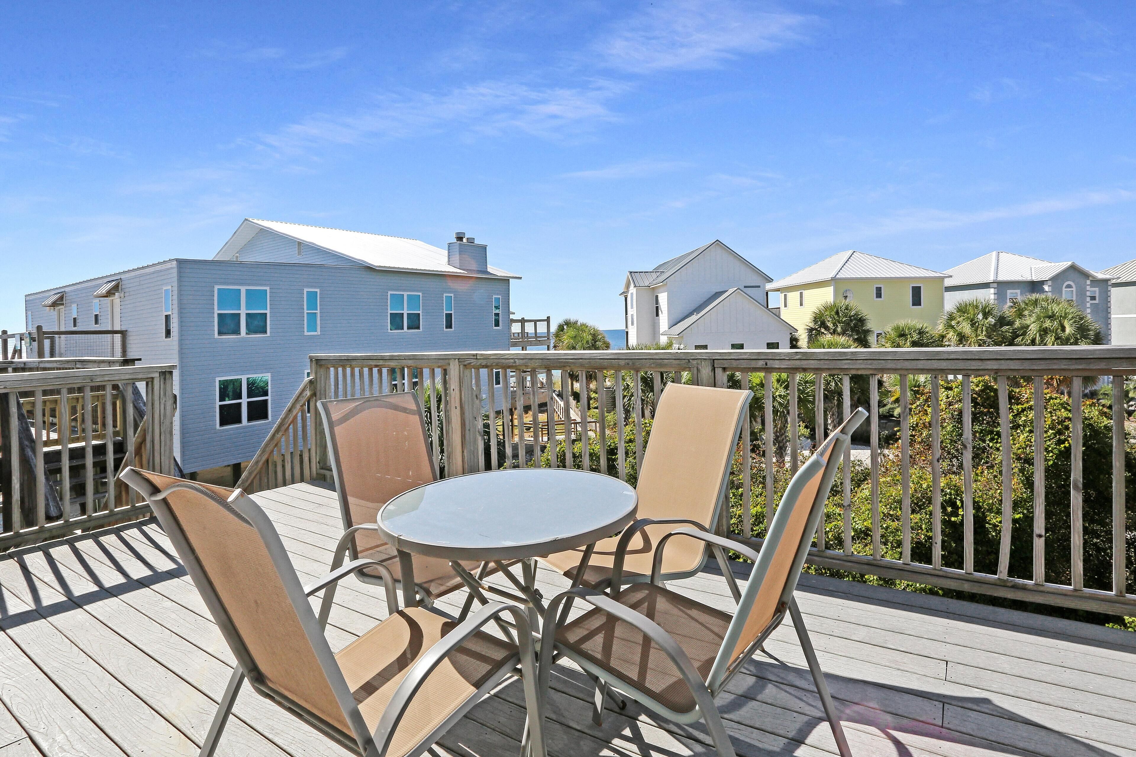 A deck with a round table and four chairs, overlooking a row of houses.