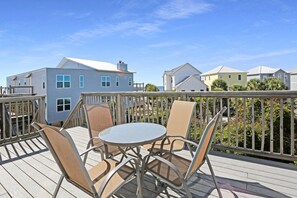 A deck with a round table and four chairs, overlooking a row of houses.