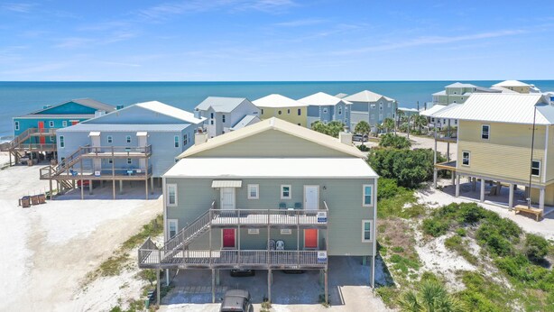 A beachfront property with multiple buildings, including a central building with a balcony and a smaller structure with a staircase. - Coastal Sunshine (Port St. Joe)