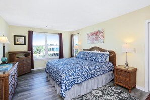 A bedroom with a large bed, a dresser, a nightstand, and a window with curtains.