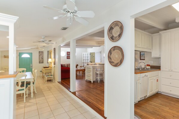 A spacious kitchen with white cabinets, a dining area with a red sofa, and a ceiling fan.