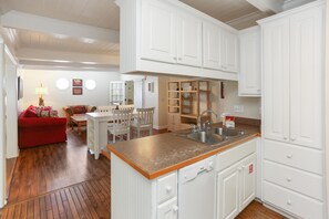 A compact kitchen with white cabinetry, a granite countertop, and a dishwasher. There is a dining area with a red sofa and a small table.