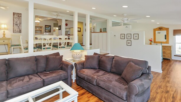 A spacious living room with a brown leather sofa, a white coffee table, and a dining area in the background. - Cape Haus (Port St. Joe)