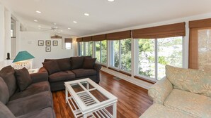 Un salón amplio con un sofá modular, una mesa de centro blanca y ventanas grandes con persianas marrones.
