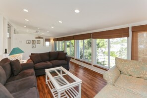 A spacious living room with a sectional sofa, a white coffee table, and large windows with brown blinds. - Cape Haus (Port St. Joe)