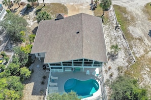A large house with a swimming pool, surrounded by trees and a paved driveway.