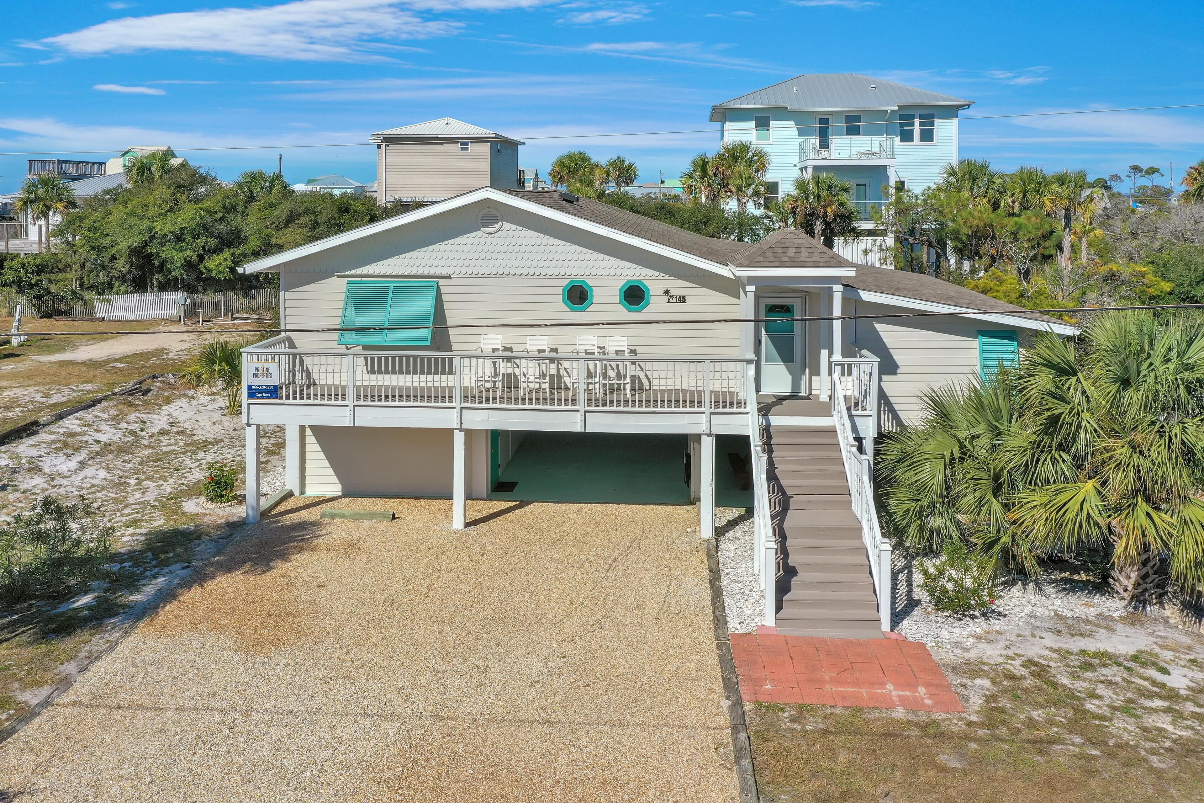 Ein Strandhaus mit überdachter Veranda, einer kleinen Terrasse und einer Treppe zum Eingang.