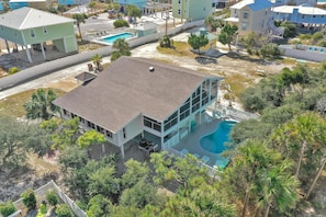 Una casa grande con piscina, rodeada de árboles y otras viviendas.