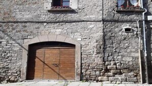 A stone building with a wooden door, arched windows, and a small balcony with flowers. - Townhome (Viterbo)