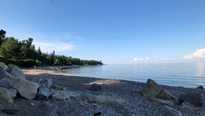 A rocky shoreline with calm water and distant trees. - Lake Life meets Country Living Near Gimli (RM of Gimli)