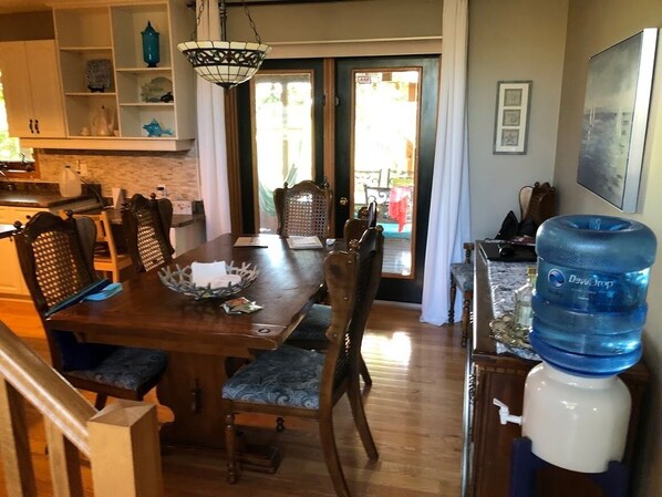 A dining area with a wooden table and chairs, a water dispenser, and a view of the outside. - Lake Life meets Country Living Near Gimli (RM of Gimli)