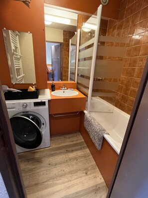 Compact bathroom with washing machine, sink, and glass-enclosed shower area.