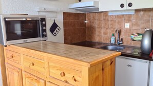 Eine kompakte Küche mit integriertem Mikrowellenherd, kleinem Kühlschrank, Holzschränken, einer Spüle und einem Herd.