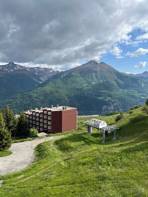 Ein mehrstöckiges Gebäude mit roter Fassade, umgeben von einer Berglandschaft mit blauem Himmel.