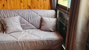 Ein graues, gepolstertes Sofa mit einer gesteppten Musterung, platziert an einer Holzwand mit Fenster und Vorhängen.