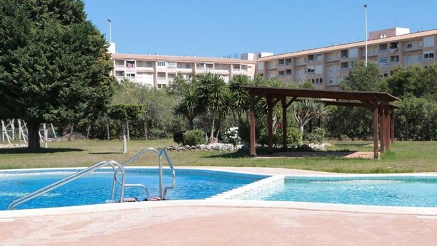 A swimming pool with a wooden pergola and a building in the background. - manewelacasa (torrevieja)