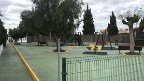 A playground with swings and a slide, surrounded by trees and a fence. - manewelacasa (torrevieja)